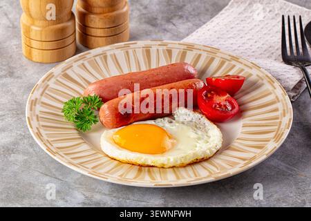 Uovo con lato soleggiato e due salsicce grigliate di pomodori ciliegini tagliati a metà su un piatto con motivi beige. Guarnire con prezzemolo fresco. Agitatori in legno con sale e pepe sul retro Foto Stock