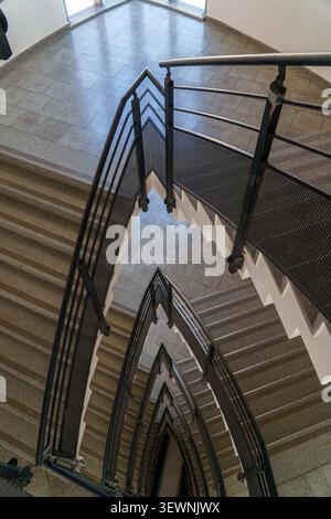 Una vista ad alto angolo che si affaccia su una scala moderna con ringhiere in mesh di metallo scuro che creano ripetuti motivi triangolari e linee geometriche. Foto Stock