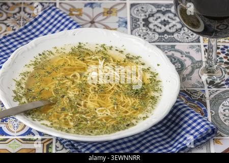 Zuppa di spaghetti con erbe aromatiche in un piatto bianco accanto a un bicchiere di vino rosso Foto Stock