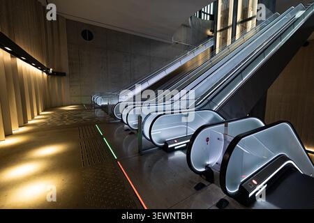 Le moderne scale mobili scorrono attraverso gli interni eleganti e minimalisti. L'illuminazione soffusa mette in risalto il cemento liscio e il pavimento a motivi geometrici. Linee pulite e tono discreto Foto Stock