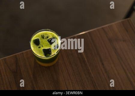 Vista ad angolo alto e dettagliata di una bevanda a strati ghiacciati con vivace tè matcha verde e succo d'arancia servito in un bicchiere trasparente su un tavolo di legno scuro Foto Stock