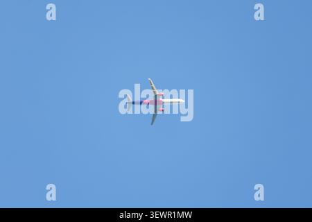 Vista dal basso di un moderno aereo commerciale per passeggeri che vola in alto in un cielo blu limpido e senza nuvole. Concetto di aviazione, viaggi e trasporto. Foto Stock