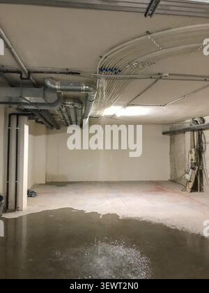 Costruzione di edifici che presentano perdite d'acqua dai tubi esposti sul pavimento di cemento, creando una grande pozzanghera e potenziali danni in un locale vuoto, Foto Stock