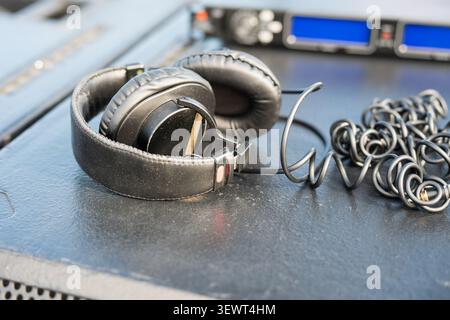 Cuffie professionali nere da studio con cavo a spirale appoggiato su un altoparlante del monitor audio su uno sfondo sfocato dell'apparecchiatura audio. Con Foto Stock
