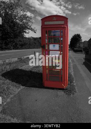 Telefono rosso convertito in Una piccola biblioteca gratuita sulla pavimentazione rurale vicino alla strada Foto Stock