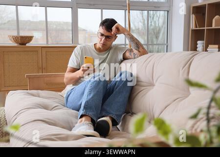 Giovane preoccupato con il telefono cellulare seduto sul divano di casa Foto Stock
