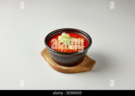 Stufato coreano di tofu sundubu jjigae servito in una tradizionale pentola nera di terracotta con tofu, kimchi e cipolla verde su sfondo grigio Foto Stock