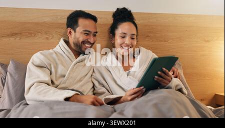 Coppia felice, online e rilassati con un tablet in camera da letto, intrattenimento e film in streaming sul sito Web. Guardare, filmare e persone con la tecnologia Foto Stock