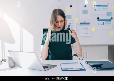 Donna d'affari che soffre di stress e frustrazione legati al lavoro, sente mal di testa e burnout da compiti travolgenti mentre lavora sul suo notebook Foto Stock