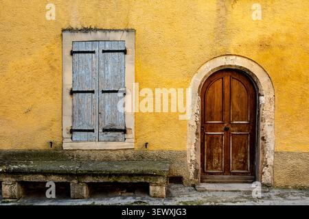 Sbarre blu pallido consumate e porta in legno ad arco su una casa ocra del villaggio di Lourmarin Provenza, Francia Foto Stock