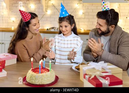 Genitori e figlia festeggiano il compleanno a casa con torta, candele, regali, gioia Foto Stock