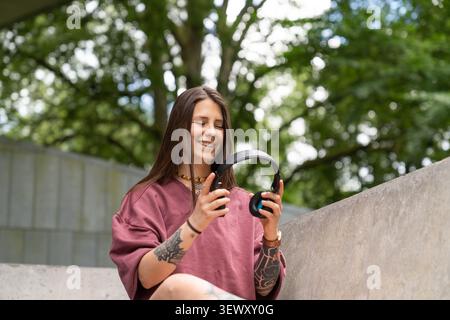 Giovane donna sorridente che tiene le cuffie all'aperto per il tempo libero Foto Stock