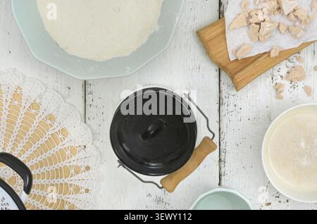Ingredienti per preparare l'impasto a base di lievito. La farina, l'acqua e il lievito sono sparsi sul tavolo di legno. C'è una lattina di latte con un coperchio nero al centro. Foto Stock
