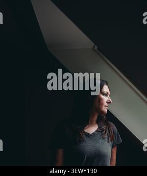 Una donna pensiva all'ombra guarda verso la luce della finestra Foto Stock