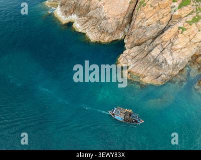 Vista aerea di una piccola barca da pesca sulle acque turchesi accanto alle scogliere rocciose di Eo Gio, Quy Nhon, Gia Lai, Vietnam. Foto Stock