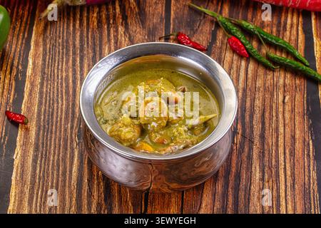 Curry verde indiano tradizionale con gamberi in karahi metallico. Vista dall'alto del piatto di pesce piccante su sfondo di legno scuro con peperoncino rosso e verde fresco Foto Stock