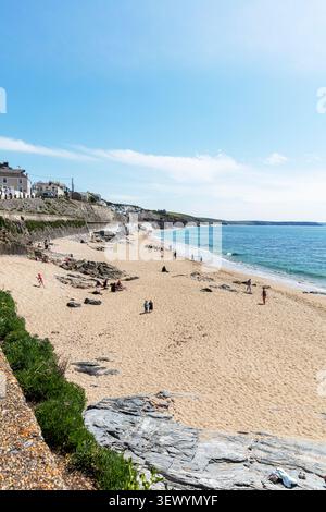 Scena in spiaggia a Porthleven, Cornovaglia, che mostra le persone che si rilassano e camminano sulla costa sabbiosa accanto alle calme acque blu. Le case si trovano sopra la pietra S. Foto Stock