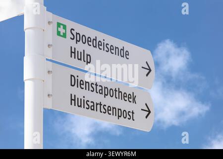 Cartello stradale con il testo olandese per "cure Emercengy" e "Apothecary, Family Doctor Medical Center" di fronte a un cielo blu Foto Stock