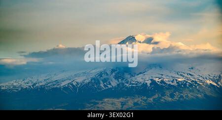 Le cime innevate si innalzano sopra nuvole nebbiose. La luce soffusa si illumina su creste distanti Foto Stock