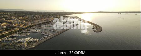 Vista aerea di un porticciolo al tramonto con barche ancorate lungo la costa durante l'ora d'oro. Golfe-Juan, Francia Foto Stock