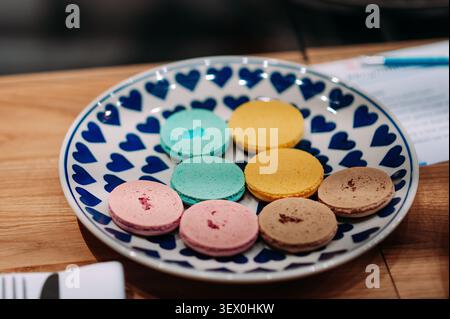 Macaron francesi colorati su piatto in ceramica decorativa durante il laboratorio di cottura Foto Stock