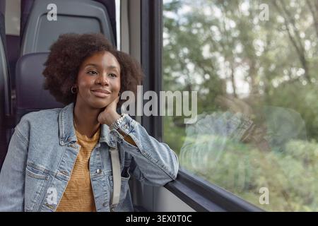 Una donna afroamericana guarda fuori dal finestrino di un treno. Le piace viaggiare e godersi la vista all'aperto. Foto Stock