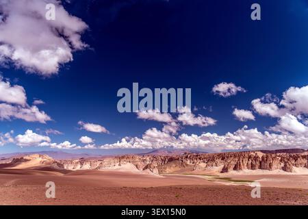 Vasto e arido paesaggio altopiano del deserto ad alta quota caratterizzato da formazioni rocciose ignimbrite sotto un suggestivo cielo blu con soffici nuvole bianche Foto Stock