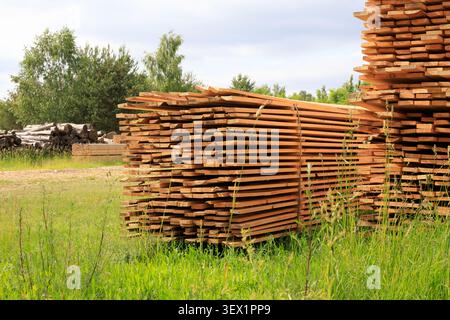 Struttura di tavole di legno impilate sullo sfondo di pannelli rustici di recinzione. Tavole di legno appena raccolte per la costruzione e la produzione Foto Stock