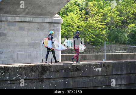 Due surfisti che trasportano tavole da surf che camminano sotto un ponte Foto Stock