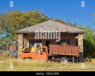 Vecchi camion parcheggiati sull'erba davanti all'edificio abbandonato in pietra con tetto in latta a Seymour, Texas Foto Stock