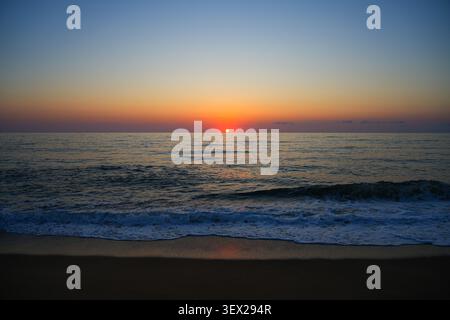 Tramonto sul mar mediterraneo con onde infranti e schiuma bianca sulla spiaggia di Piscinas in Sardegna, Italia Foto Stock