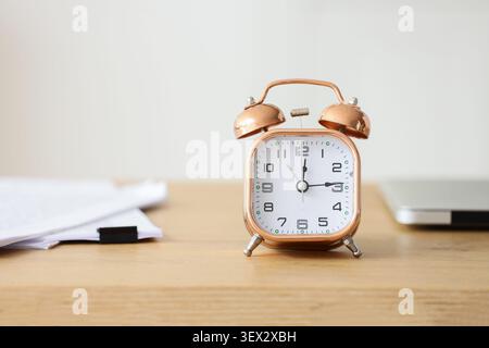 Sveglia in rame su scrivania in legno con carta e computer portatile Foto Stock