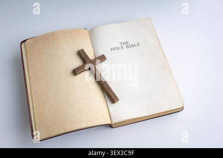 Crucifx croce in cima a una Sacra Bibbia aperta. Isolato su sfondo chiaro. Foto Stock