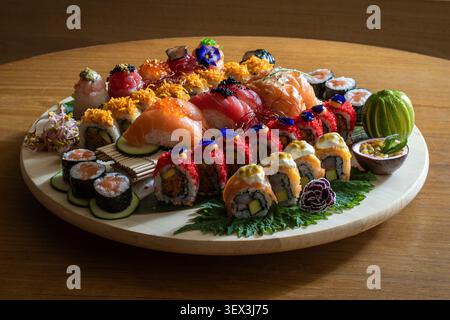 Un piatto di sushi splendidamente organizzato con una varietà di panini e nigiri su una superficie rotonda in legno. Foto Stock