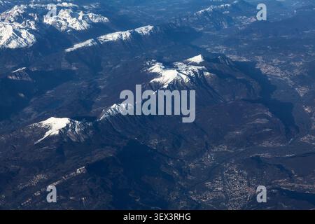 La vista aerea mozzafiato rivela le vette innevate delle Alpi e le profonde creste che si estendono su un vasto e aspro paesaggio di valli boscose scure Foto Stock