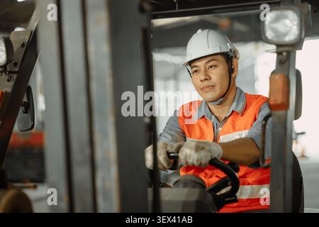 Lavoratore maschio asiatico che guida il conducente del carrello elevatore a forche di lavoro felice nell'industria del magazzino della fabbrica dello stabilimento Foto Stock