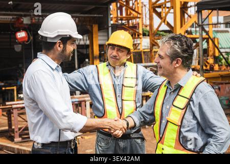 Felice uomo d'affari indiano affare progetto scuotendo la mano con l'ingegnere edile straniero costruttore sorridente cooperazione di successo. Foto Stock