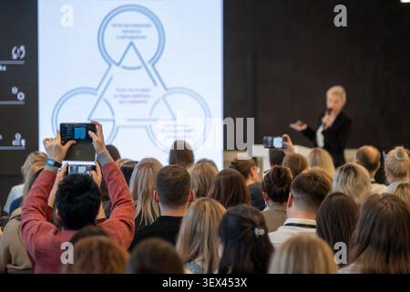 Una folla di professionisti che guardano la presentazione di un discorso di apertura alla conferenza aziendale, molte diapositive di registrazione con smartphone, speaker sul podio che presenta un diagramma visivo. Foto Stock