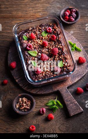 Decadente brownie al lampone al cioccolato cotto in piatto di vetro, condito con noci e menta Foto Stock
