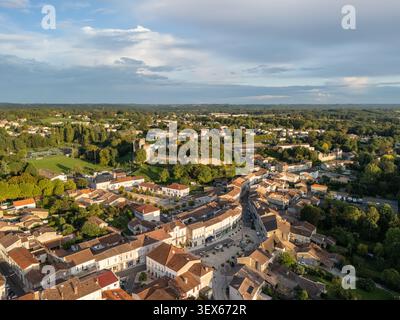 Vista aerea di un pittoresco villaggio storico con tetti in terracotta, strade tortuose e una piazza centrale adagiata tra verdi campi e alberi, Foto Stock