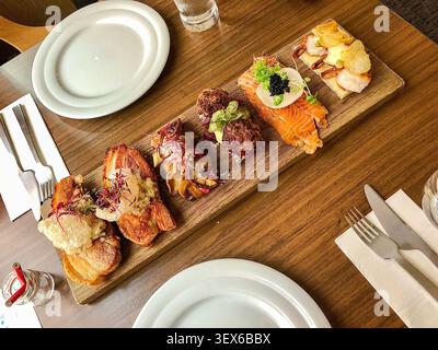 Un sofisticato piatto di antipasti gourmet su una tavola di legno, caratterizzato da una varietà di texture e tecniche culinarie raffinate per un'esperienza di degustazione. Foto Stock