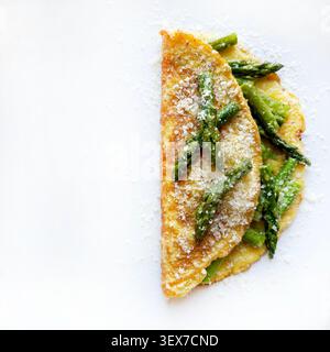 Omelette all'uovo ripiena di asparagi verdi saltati e parmigiano grattugiato. Cibo gourmet sano su sfondo bianco. Spazio di copia, vista dall'alto. Foto Stock