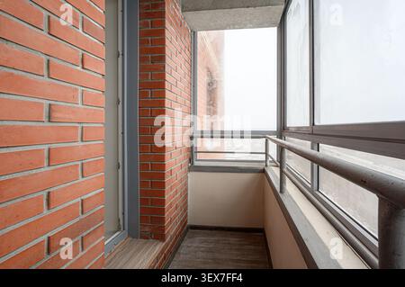 balcone con pareti in mattoni e grandi finestre, ringhiera in metallo e pavimento in cemento. La vista esterna è sfocata Foto Stock