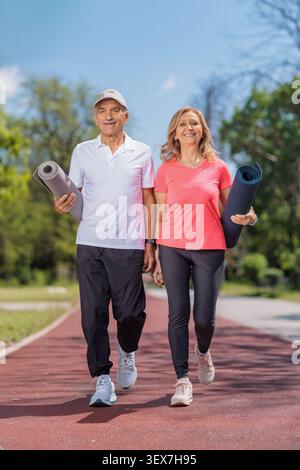 Una coppia matura attiva che cammina in un parco con materassini fitness Foto Stock