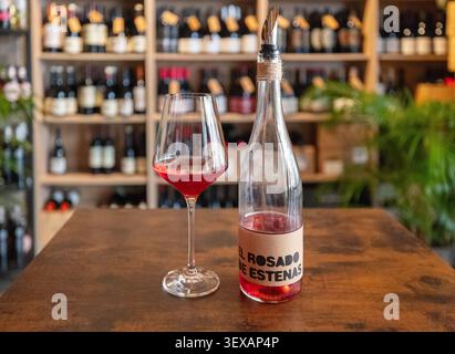 Bicchiere di vino rosa e bottiglia su un tavolo di legno all'interno della enoteca. Valencia, Spagna - 8 agosto 2025. Foto Stock