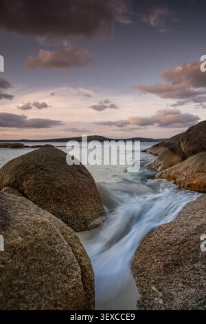 Vista di Waterfall Beach con grandi massi di granito e dolci onde che scivolano sulla sabbia bianca al tramonto ad Albany, Washington, Australia. Foto Stock