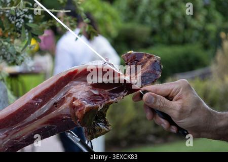 Persona che affetta una deliziosa marmellata iberica gourmet con un coltello affilato durante un evento all'aperto Foto Stock