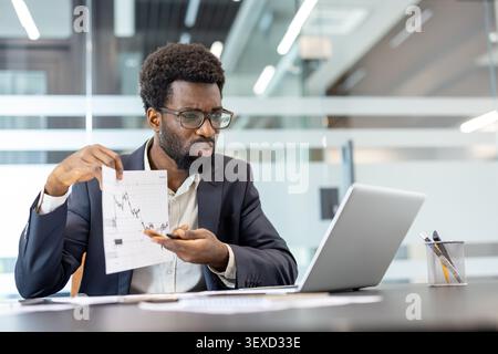 Giovane che analizza le tendenze del mercato azionario su carta mentre discute le strategie di investimento durante un incontro online in un ambiente d'ufficio contemporaneo Foto Stock