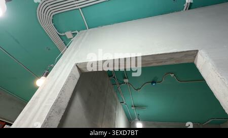 Condotti elettrici esposti e cablaggi su un soffitto dipinto di verde in uno spazio commerciale in costruzione. Foto Stock