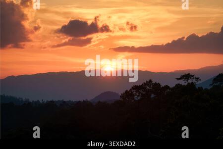 Vivace tramonto arancione con nuvole su creste di montagna a strati con alberi sagomati nella foresta tropicale Foto Stock